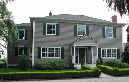 A large gray house with green shutters and bushes.
